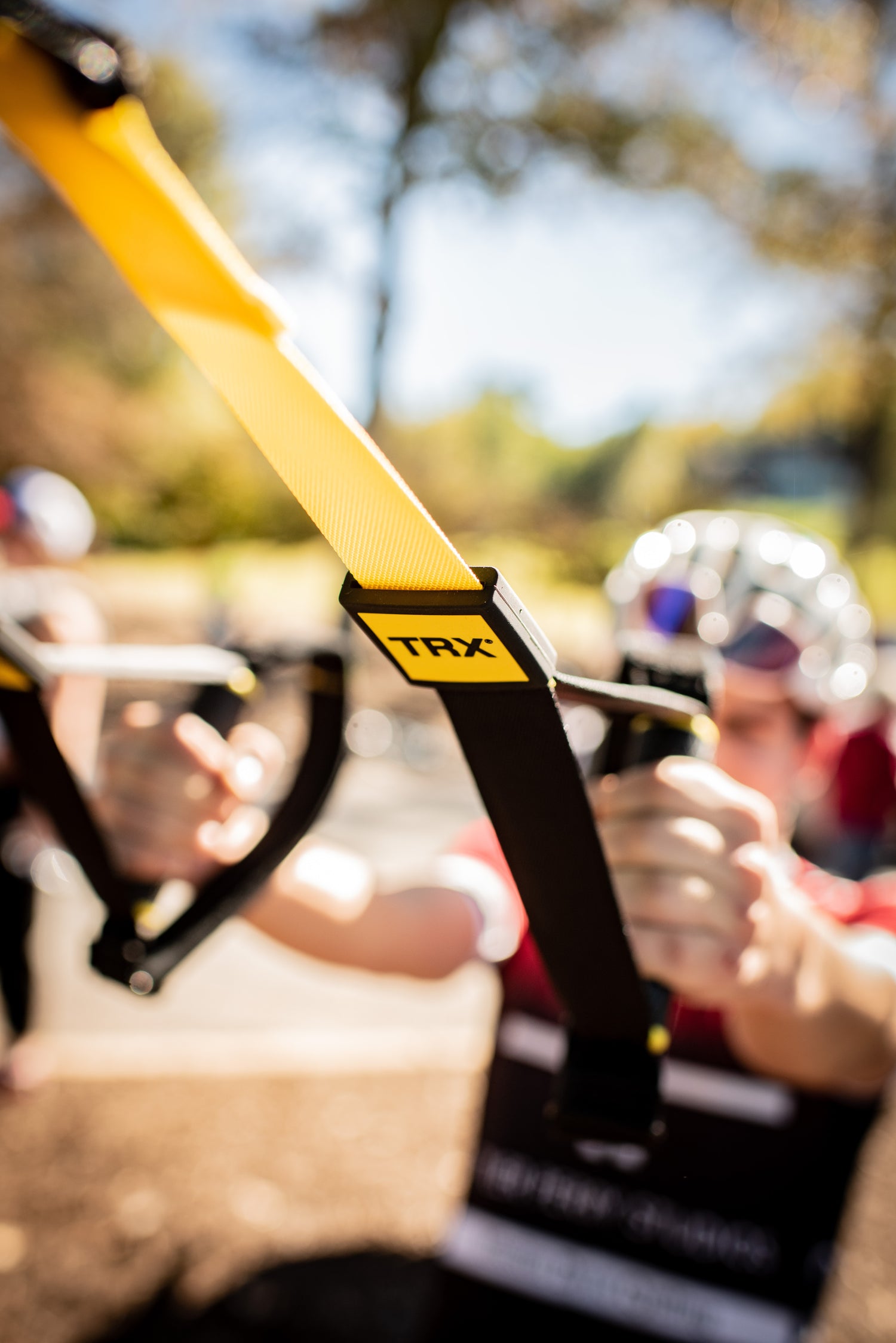 A cyclist wearing a riding kit, helmet, and sunglasses warms up outside using the TRX Suspension Trainer.
